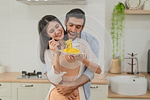 Happy young couple cooking together in the kitchen, feeding each other in their kitchen at home