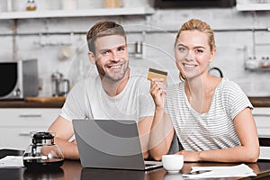 happy young couple with credit card using laptop and smiling at camera