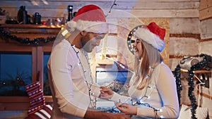 Happy young couple dancing with christmas lights and santa hats. Love and affection during the christmas eve