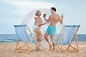 Happy young couple dancing near deck chairs at beach