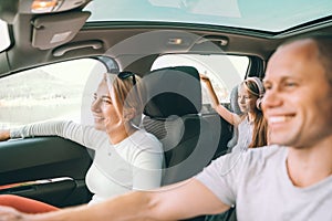 Happy young couple with daughter inside the modern car with panoramic roof during auto trop. They are smiling, laughing during photo