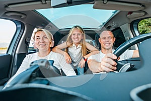 Happy young couple with daughter inside the modern car with panoramic roof during auto trop. They are smiling, laughing during photo