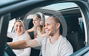 Happy young couple with daughter inside the modern car with panoramic roof during auto trop. They are smiling, laughing during photo