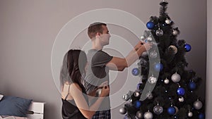 Happy young couple decorating Christmas tree. Young family decorating Christmas tree. Modern, loft interior room. Loving