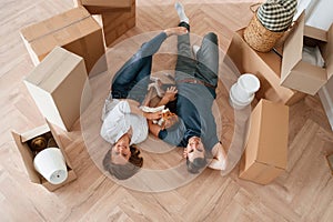 Happy young couple with dog are moving to new home. Lying down on the floor