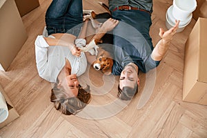 Happy young couple with dog are moving to new home. Lying down on the floor