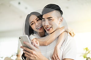 Happy young couple embracing while looking at mobile phone in living room at home