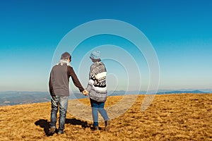 Happy young couple enjoying nature at mountain peak. Loving couple holding hands over blue sky background. Love, freedom, dream