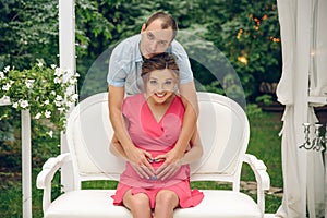 Happy young couple expecting baby, pregnant woman with husband touching belly, sitting on white sofa