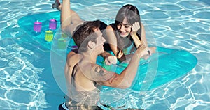 Happy young couple floating on mattress in pool