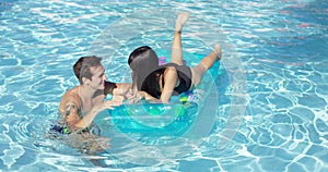 Happy young couple floating on mattress in pool