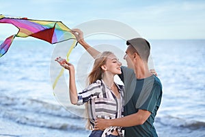 Happy young couple flying kite near sea