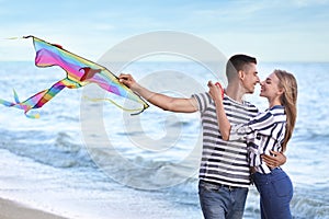 Happy young couple flying kite near sea