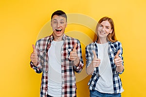 Happy young couple of friends, man and woman, showing thumb up gesture on yellow background