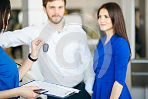 Happy young couple getting keys of their new car at dealership