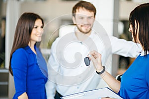 Happy young couple getting keys of their new car at dealership