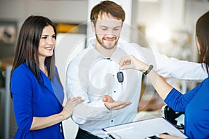 Happy young couple getting keys of their new car at dealership