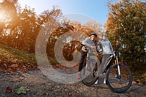 Happy young couple going for a bike ride on an autumn day in the park, backlight.