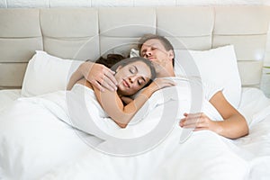 Happy young couple handsome man and beautiful woman lying in bed in bright bedroom in the morning family idyll