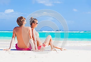 Happy young couple in hats sitting on a tropical beach in Barbados