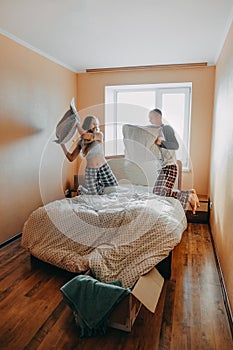 Happy young couple is having fun in bed in new empty home. Enjoying the company of each other. Pillow battle. Valentine`s Day