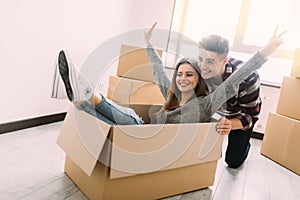Happy young couple is having fun with cardboard boxes in new house at moving day.