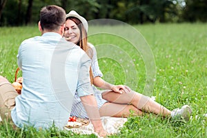 Happy young couple having a great time in a park, sitting on a picnic blanket