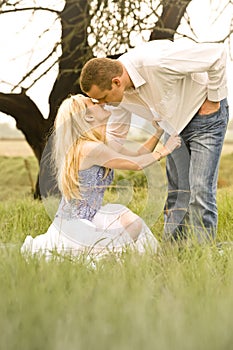 Happy young couple having a romantic kiss outdoors in green field