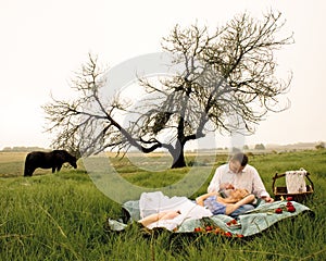 Happy young couple having a romantic picnic outdoors in green field