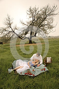 Happy young couple having a romantic picnic outdoors in green field
