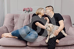 Happy young couple is havinggreat time on pink sofa in their living room with their pet Yorkshire Terrier.Concept of happy family