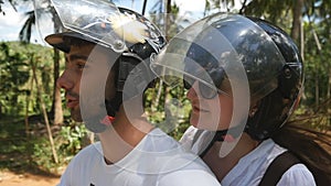 Happy young couple in helmets rides an motor scooter along country road. Smiling man and woman drives a moped along