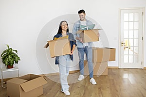 Happy young couple holding carton boxes and walking in their new apartment