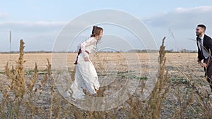 Happy young couple holding hands run through a wide field, having fun outdoors. Countryside. Man and woman running on