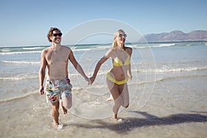 Happy young couple holding hands while running at beach