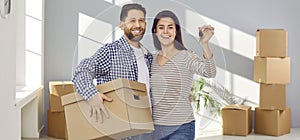 Happy young couple holding a key and cardboard boxes standing in a new apartment on moving day.