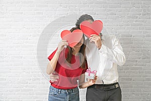 Happy young couple is holding red paper hearts and smiling on blick wall background