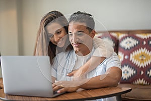 Happy young couple at home using laptop together surfing the web. Concept of new life and love. Indoor leisure activity with