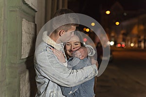 Happy young couple is hugging, evening city background. Guy hugs and kiss his girlfriend. Romantic date on the street