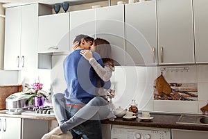 Happy young couple hugging on kitchen. Woman sitting on table.