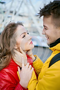 Happy young couple hugging and looking at each other with smile, wearning in bright yellow and red down jackets.