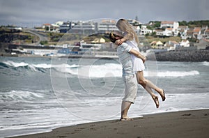 Young woman in white dress watching sea waves on Sao Miguel beach with black voncanic sand, AzoresHappy young couple on windy beac photo
