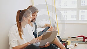 Happy young couple with laptop planning repair in their new house. Satisfied young couple look at laptop planning new