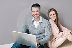 Happy young couple with laptop sitting on floor. Online education or shopping