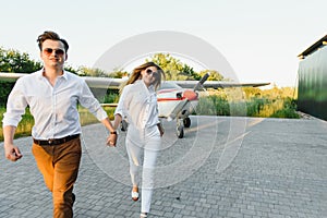 Happy young couple laughing and having fun on runway near private aircraft