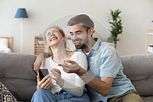 Happy young couple laughing holding phone talking about online joke