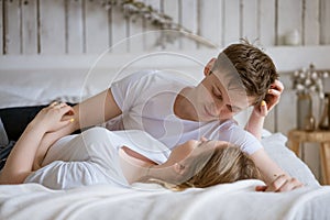 Happy young couple lie in bed and hug each other on white bed linen, look