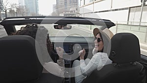 Happy young couple listening to music while driving cabriolet car in the city