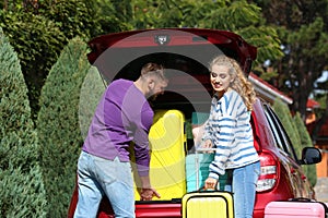 Happy young couple loading suitcases in car trunk