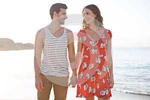 Happy young couple looking at each other while holding hands at beach